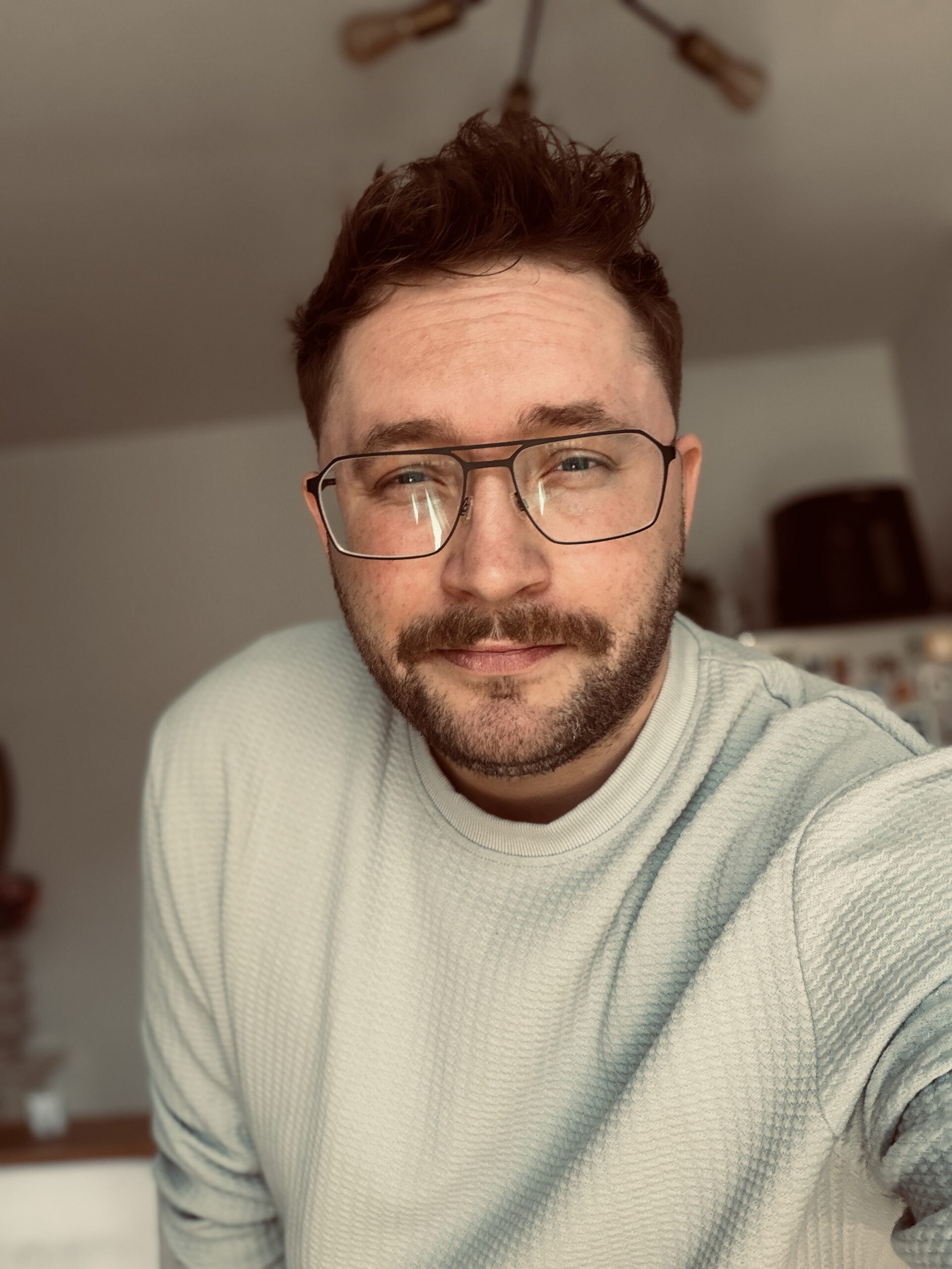 Eine Nahaufnahme von Christoph Hampe, der in einem hellen, strukturierten Pullover und mit Brille entspannt direkt in die Kamera blickt. Das Bild hat eine warme Farbgebung.